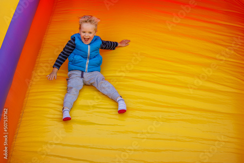 Obraz na plátně Happy little boy sliding down an a yellow- orange inflatable slide