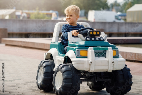 Close up portrait of young happy kid driving electric toy car outdoors. photo