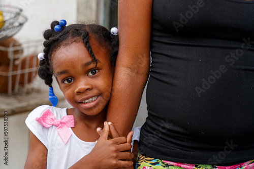 Konstfotografi A little Haitian girl stands next to her mother.