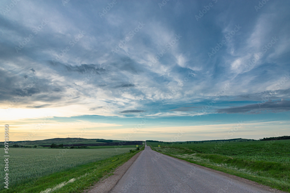 Road with green grass on the side and clouds at sunset.