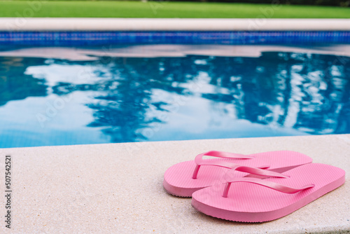  Pink flip flops for pool or beach on grass with pool bottom. Pool water texture. to use text. summer objects.
