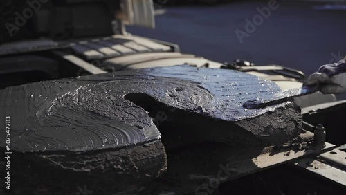 A worker hand smearing trailer fifth wheel coupling with lubricant oil. Semi-truck mechanical maintenance 