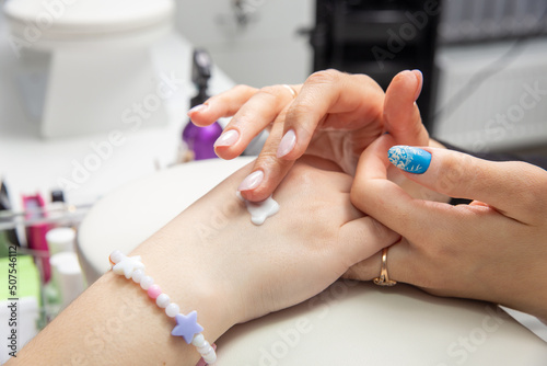 A manicurist applies hand cream to female hands after a hardware manicure in a beauty salon.