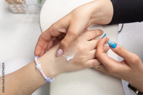 A manicurist applies hand cream to female hands after a hardware manicure in a beauty salon.