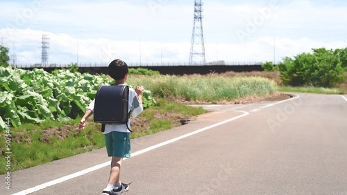 田舎道を歩いて学校に登校する小学生の男の子