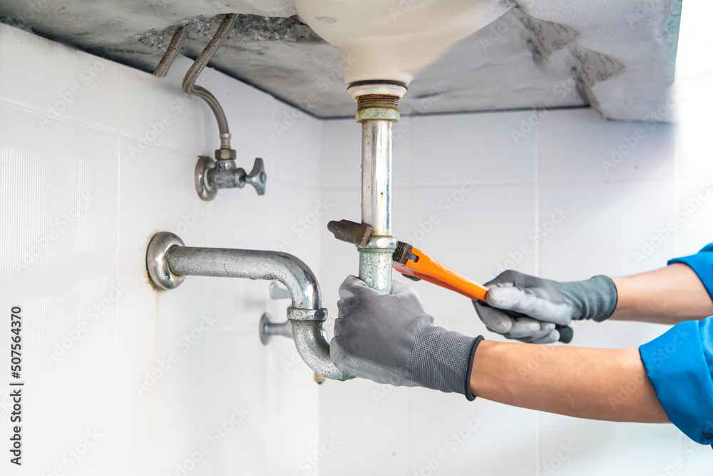 Technician plumber using a wrench to repair a water pipe under the sink. Concept of maintenance, fix water plumbing leaks, replace the kitchen sink drain, cleaning clogged pipes is dirty or rusty. Technician plumber using a wrench to repair a water pipe under the sink. Concept of maintenance, fix water plumbing leaks, replace the kitchen sink drain, cleaning clogged pipes is dirty or rusty.