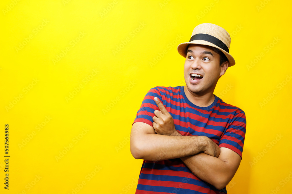Portrait of cheerful asian man in basic clothing Casual wear red striped T-shirt and wear a hat smiling and show giving thumbs up at camera with showing success. isolated over yellow background.
