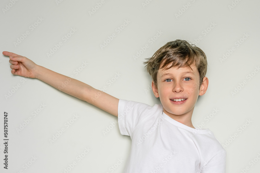 White caucasian boy 9 years old against a white wall and happily points his hand to the side White caucasian boy 9 years old against a white wall and happily points his hand to the side