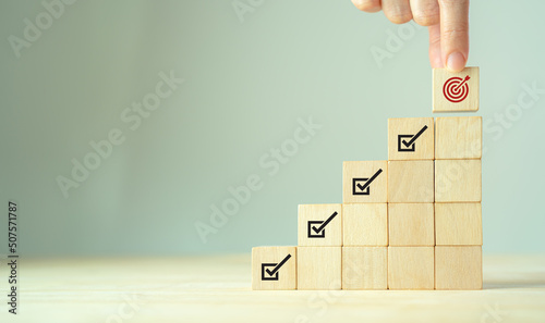 Corporate regulatory and compliance. Goals achievement and business success. Project and goals tracking. Task completion. Managing project timeline. Holding wooden cube with target achievement icon.