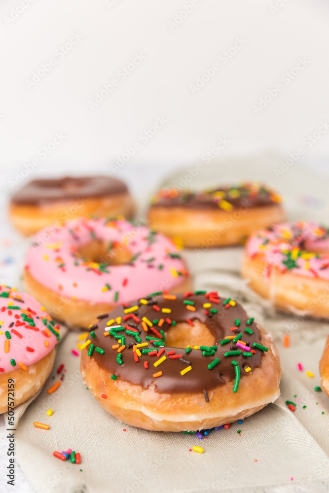 There are several strawberry and chocolate sprinkled donuts in different spots on a green napkin. There are several strawberry and chocolate sprinkled donuts in different spots on a green napkin.