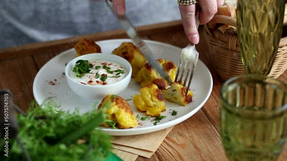 Women's hands with a knife and fork.Cauliflower in batter with white spicy sauce Women's hands with a knife and fork.Cauliflower in batter with white spicy sauce