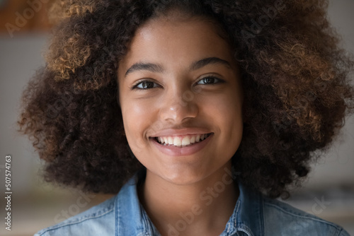 Closeup face attractive optimistic African teen lady look at camera with perfect white smile promote dental care show medical whitening procedure result. Happy young woman talk to friend in video chat