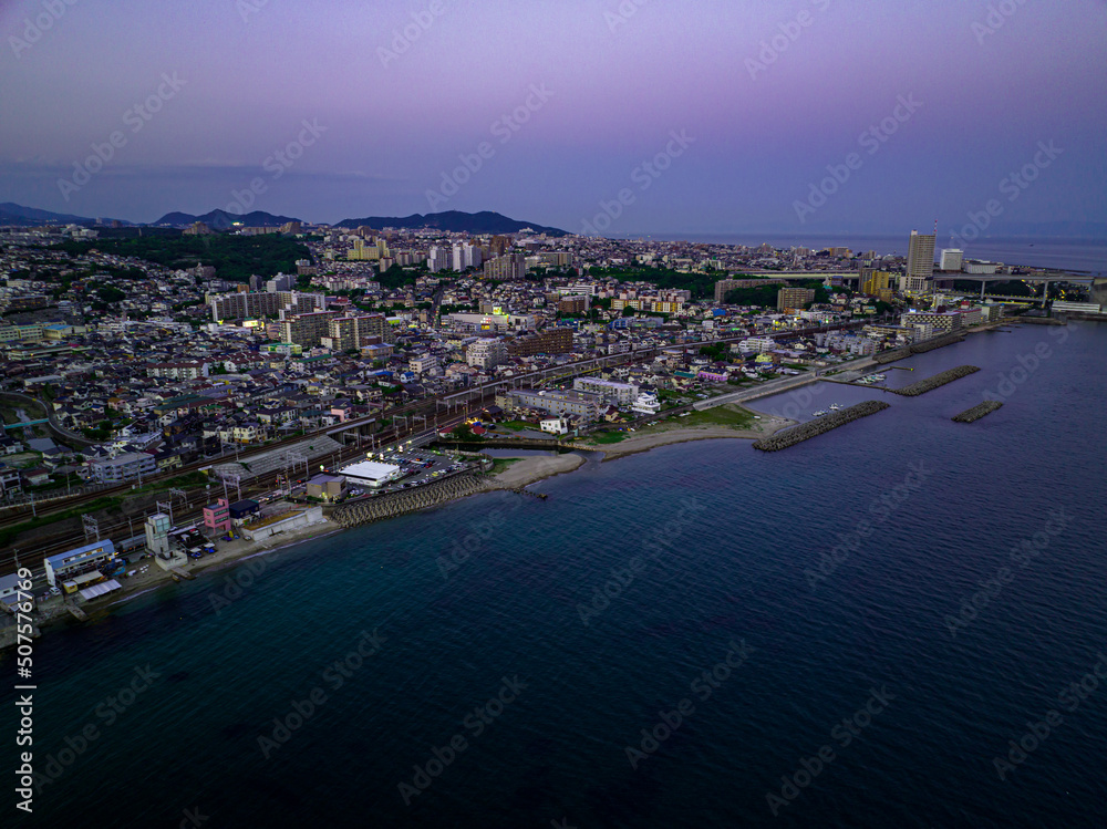 Fototapeta premium Aerial view of post-sunset glow over coastal town on point