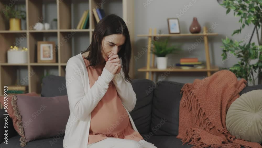 Caucasian pregnant woman feeling stress and anxiety while sitting alone on sofa. Young expectant mother thinking about upcoming birth of child. Caucasian pregnant woman feeling stress and anxiety while sitting alone on sofa. Young expectant mother thinking about upcoming birth of child.