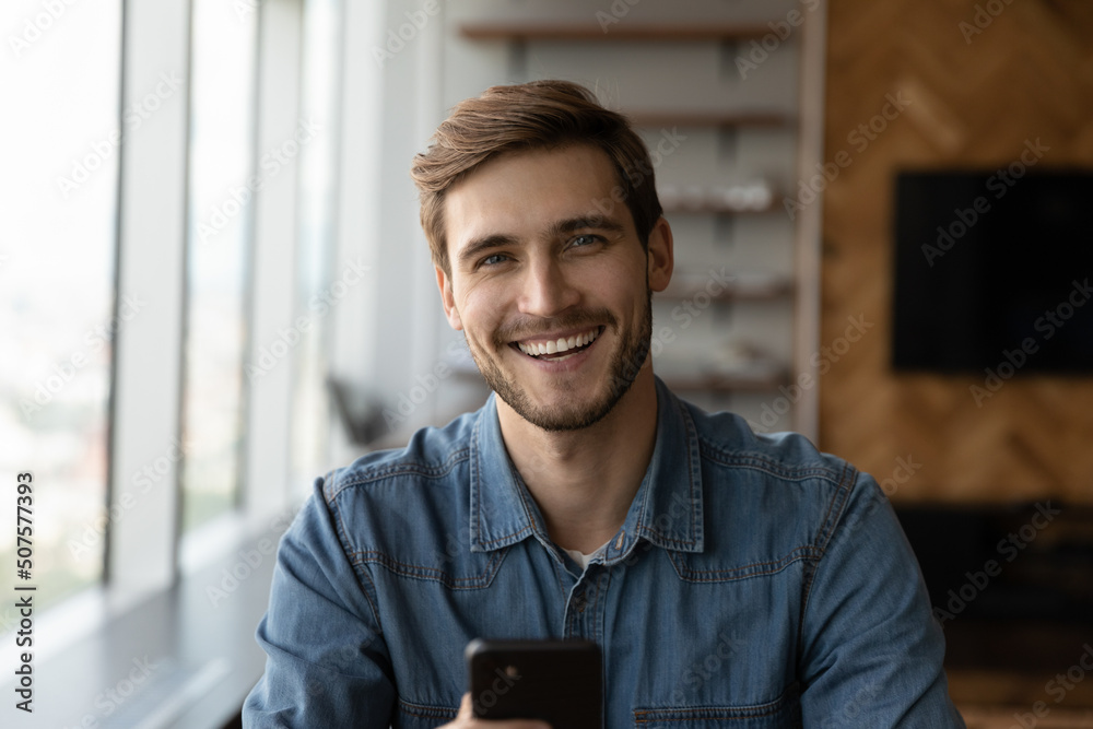 Head shot of happy young millennial man holding smartphone, looking at camera, smiling, laughing. Portrait of positive customer, smartphone user satisfied with online app, virtual service work - obrazy, fototapety, plakaty 