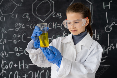 serious scientist child with glasses in lab coat with chemical flasks having an idea, school blackboard background with hand drawn formulas