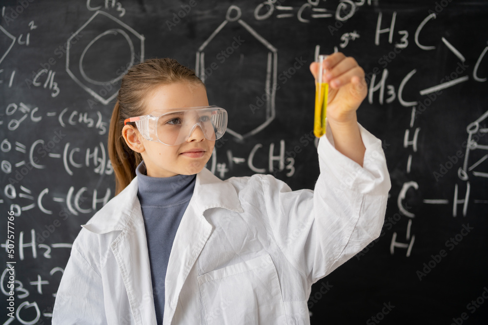 Education concept. little children scientists look at an Erlenmeyer flask containing chemicals to conduct experiments in the laboratory, student girl in a white coat blackboard