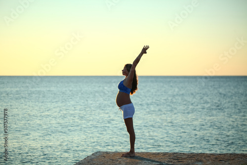 pregnant girl doing yoga on the seashore in the morning against the sky and water © Elroi