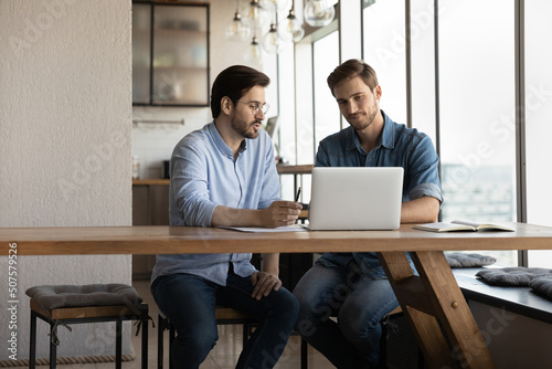Corporate mentor explaining content on laptop to intern, training new employee, telling about work on startup. Client consulting manager, negotiating on project, watching design on screen