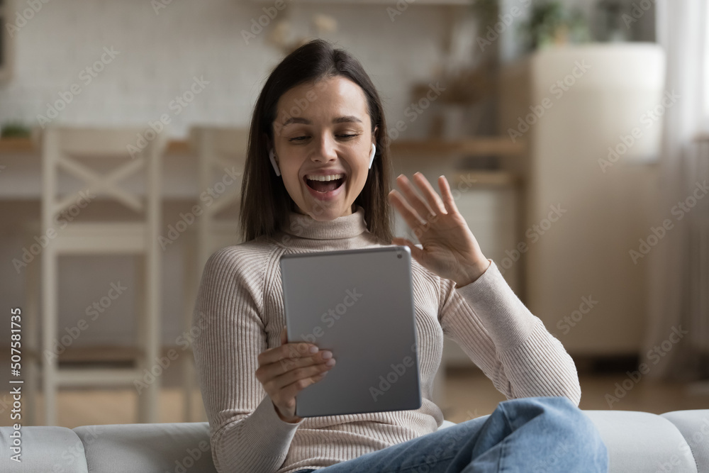 Positive excited millennial tablet user girl with wireless earbuds in ears talking on video call, waving greeting hand, saying hello, smiling, laughing, speaking. Woman chatting on online conference Positive excited millennial tablet user girl with wireless earbuds in ears talking on video call, waving greeting hand, saying hello, smiling, laughing, speaking. Woman chatting on online conference