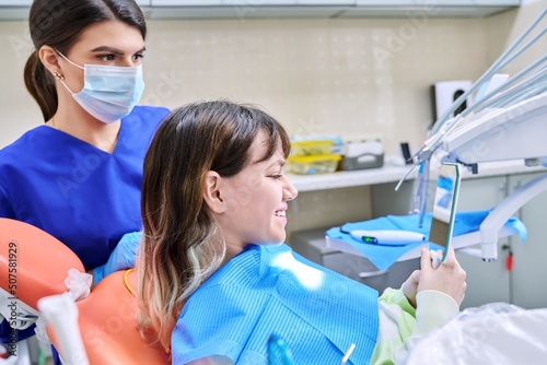 Teenage female looking at healthy teeth in mirror, in dental office