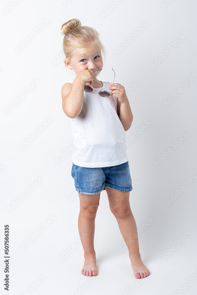 Beautiful child holding sunglasses posing on a light background in the studio Beautiful child holding sunglasses posing on a light background in the studio