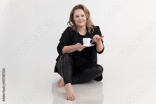 Blonde smiling and confident barefoot woman holding hot cup of coffee or tea by hand with little finger. White back view photo