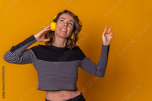 Caucasian girl listening to streaming music and smiling and dancing with her phone, headphones, yellow background