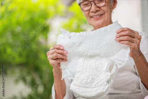 Happy smiling asian senior woman showing disposable diaper for adult,looking at nappy pamper with satisfaction,old elderly patient with urinary incontinence,consumer goods,health care concept