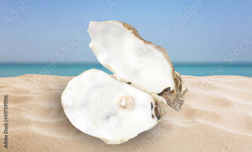 Open oyster shell with white pearl on sandy beach near sea