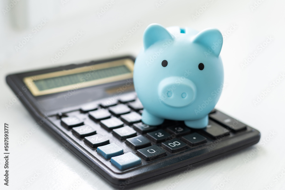 Piiggy bank with calculator close-up on blue pastel background. Calculation of the family budget, saving. Minimalism. Piiggy bank with calculator close-up on blue pastel background. Calculation of the family budget, saving. Minimalism.