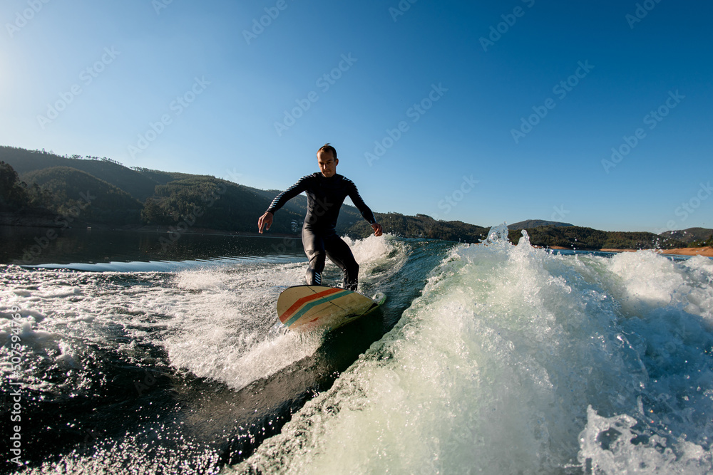 male wakesurfer riding down the splashing wave on blue sky background male wakesurfer riding down the splashing wave on blue sky background