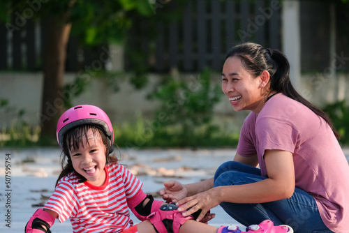 Asian mother helps daughter practice roller skating in the park. Exciting outdoor activities for kids.
