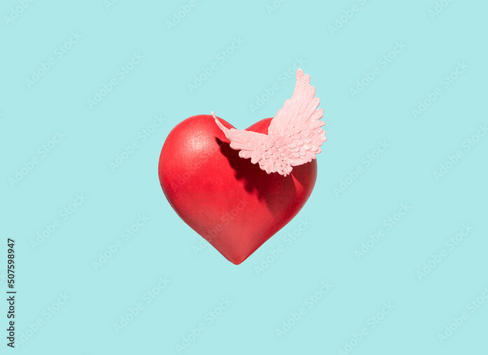 Red heart and pastel pink wings. Creative conceptual arrangement against pastel blue background. Free love idea. Red heart and pastel pink wings. Creative conceptual arrangement against pastel blue background. Free love idea.