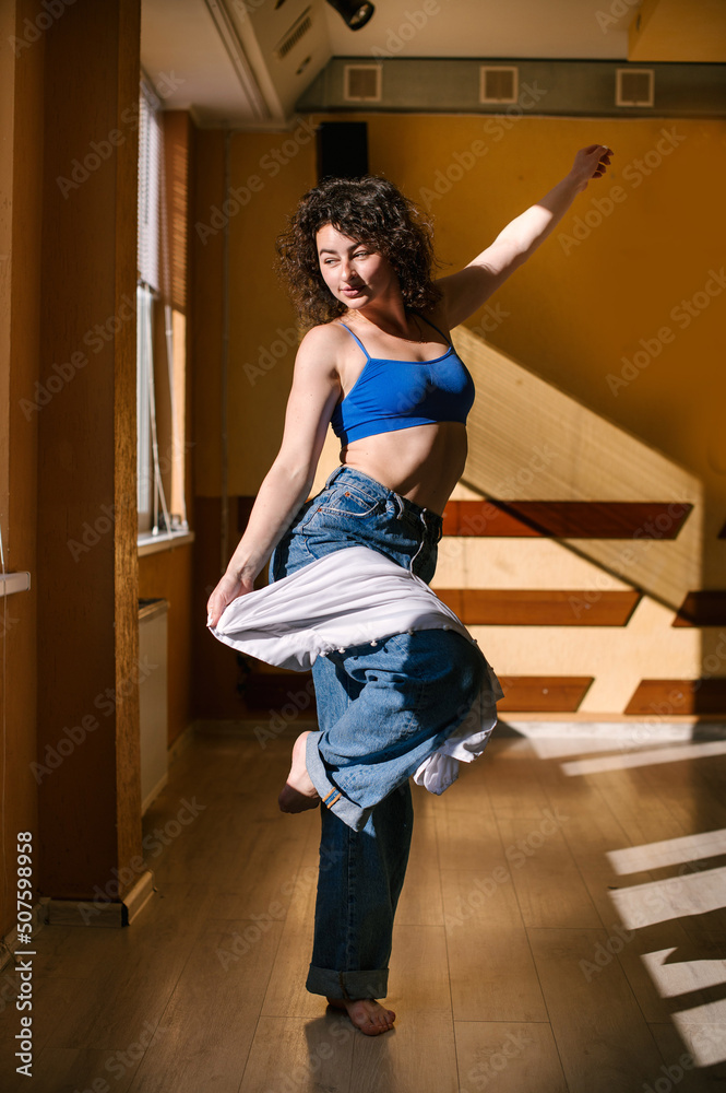 Young woman dancer is dancing modern dance in dancing hall with beautiful harsh dramatic light