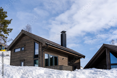 Wooden holiday home in the mountains of Norway in winter, where there is a lot of white snow and fluffy white clouds in the beautiful blue sky
