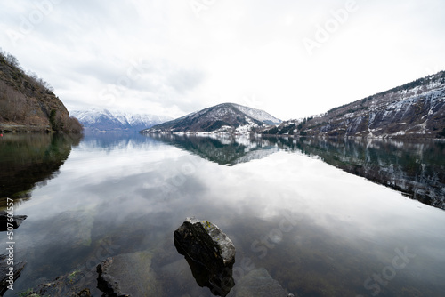 Norwegian fjord in early spring when there is still snow in the mountains and the dark water of the fjord is like a mirror reflecting all the mountains and the sky photo