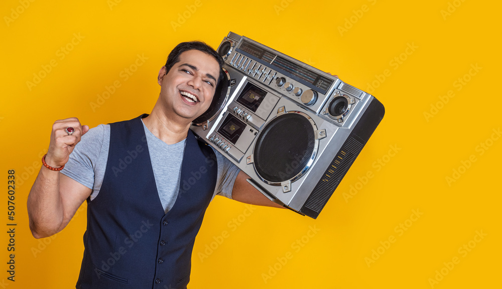 The guy listens to music. The man is delighted with music. The guy dances to the beat of the melody. The man holds a large tape recorder. The concept of the musical style of the 80s. - obrazy, fototapety, plakaty 