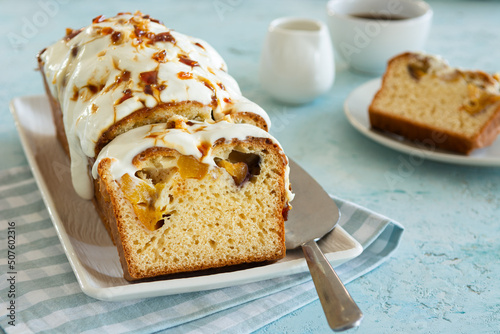 Piece of pound cake with fruit, cream icing and caramel served on a plate with a spatula on a blue textured background. Coffee break concept