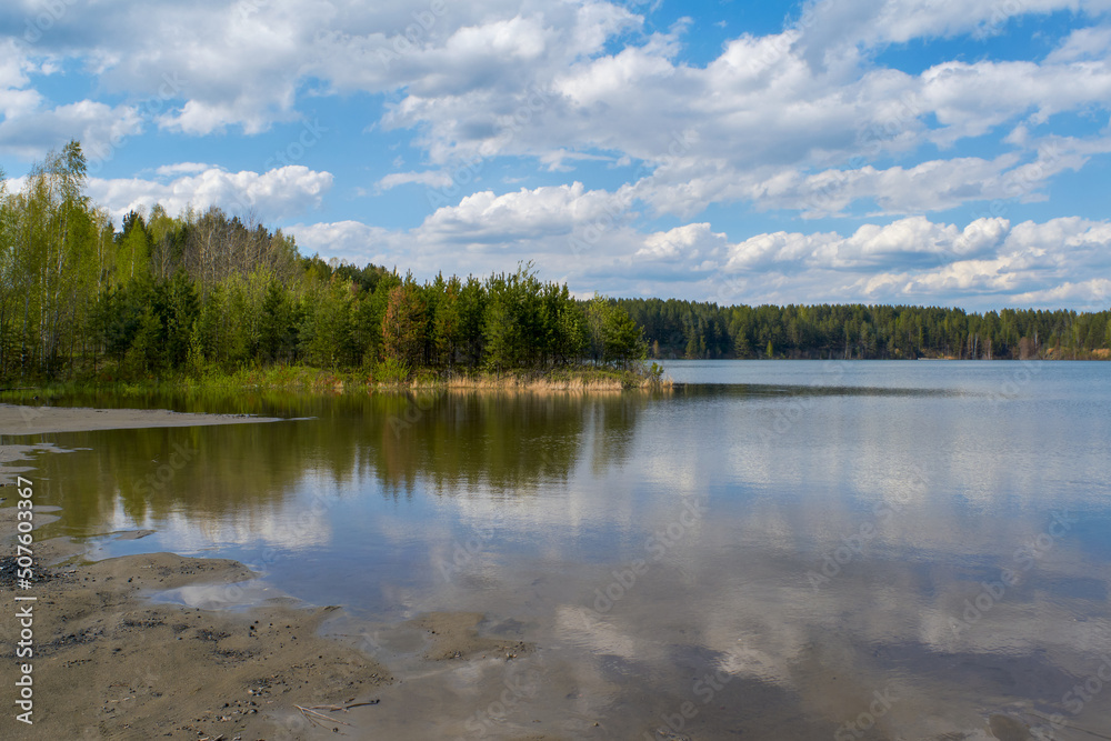 Scenic view at beautiful spring day on a forest lake. Deep blue cloudy sky and forest on a background, spring landscape.