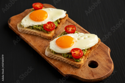Homemade Healthy Egg, Avocado and Tomato Toast on a rustic wooden board, side view.