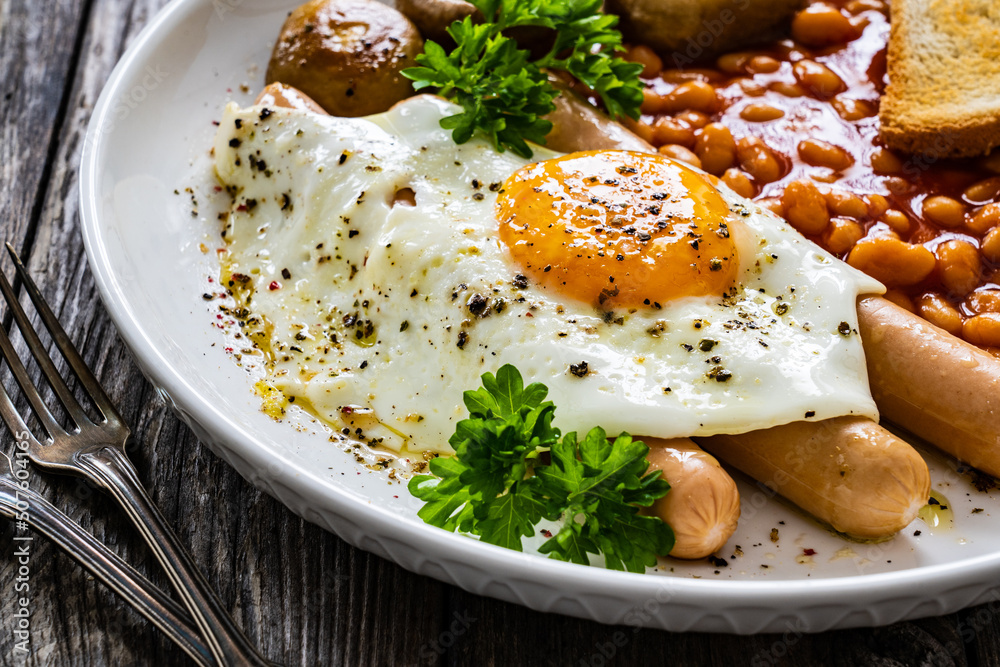 English breakfast - toast, egg, sausages, beans in tomato sauce and mushrooms on wooden table
