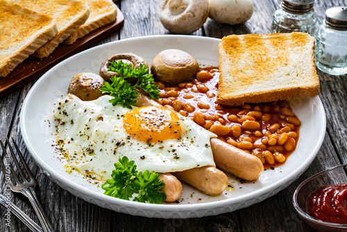 English breakfast - toast, egg, sausages, beans in tomato sauce and mushrooms on wooden table
 photo