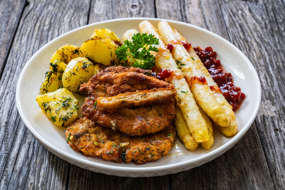 Fried schnitzel and white boiled asparagus with potato served on wooden table
