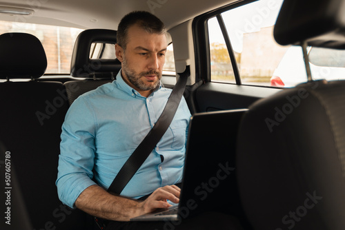 Businessman using laptop while going by car © Prostock-studio