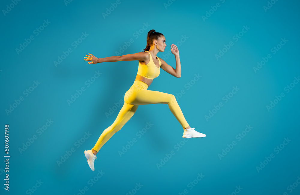 Athletic Woman Jumping Posing In Mid Air Over Blue Background