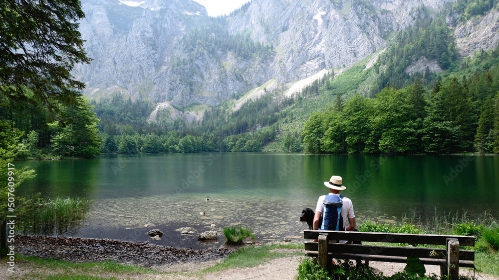A Man Is Sitting On A Bench In Front Of A Lake A Man Is Sitting On A Bench In Front Of A Lake