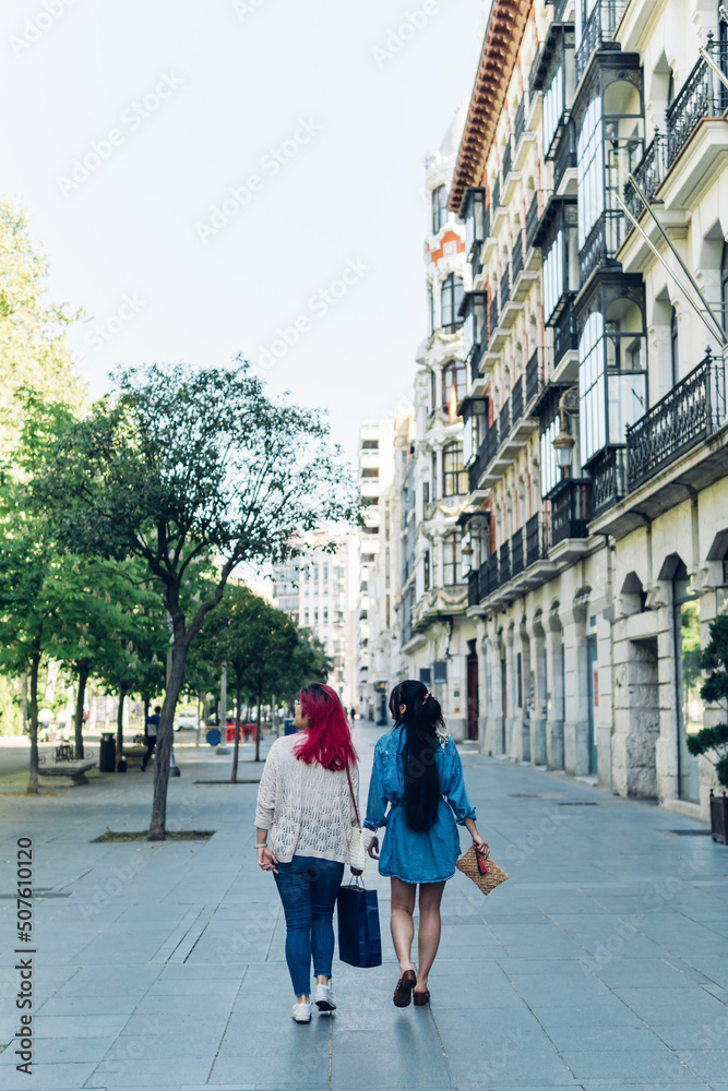 Vertical shot of two unrecognizable women back to back with bags walking around the city.
