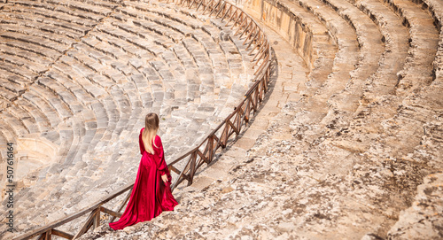 Adventure photo tourist woman in red dress on background Amphitheater in Hierapolis ancient city Pamukkale Turkey