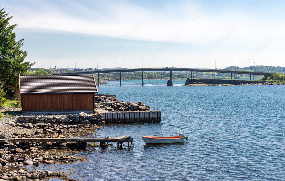 Rocky beach with a short wooden jetty and a small fishing boat near Hafrsfjord bridge, Tananger, Norway, May 2018